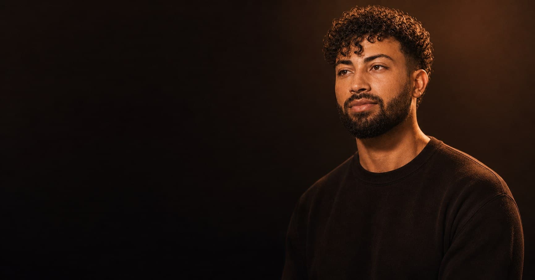 Studio portrait of Gian against a deep obsidian backdrop, warm rim light catching the right side of his face.